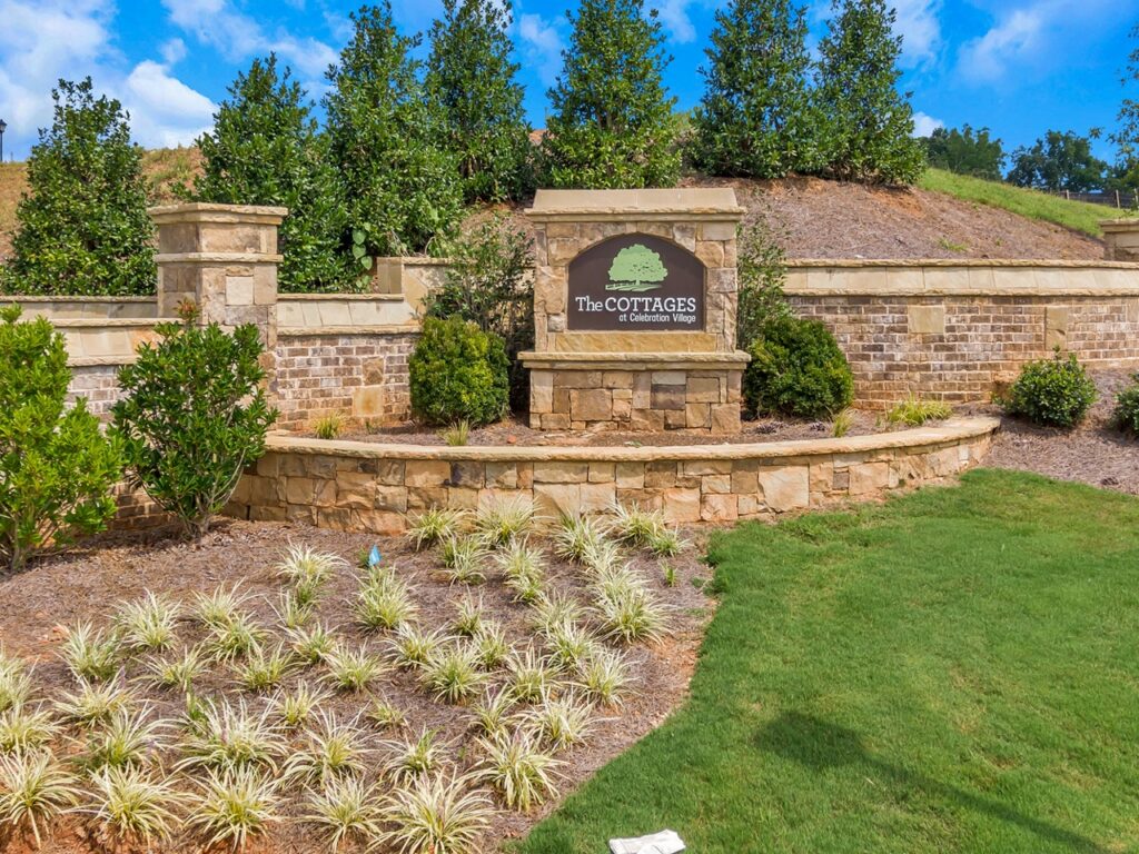 A photo of the brown brick entry sign to the cottages that says "The Cottages at Celebration Village" and features trees in the background near Cumming, GA at Celebration Village Forsyth.