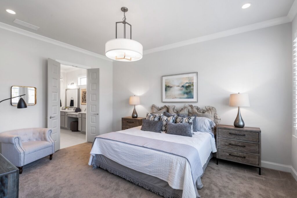 A photo of the large Master Bedroom showing the bed with bedside tables and lamps on each side  at Celebration Village Forsyth, a senior living community near John's Creek, GA.
